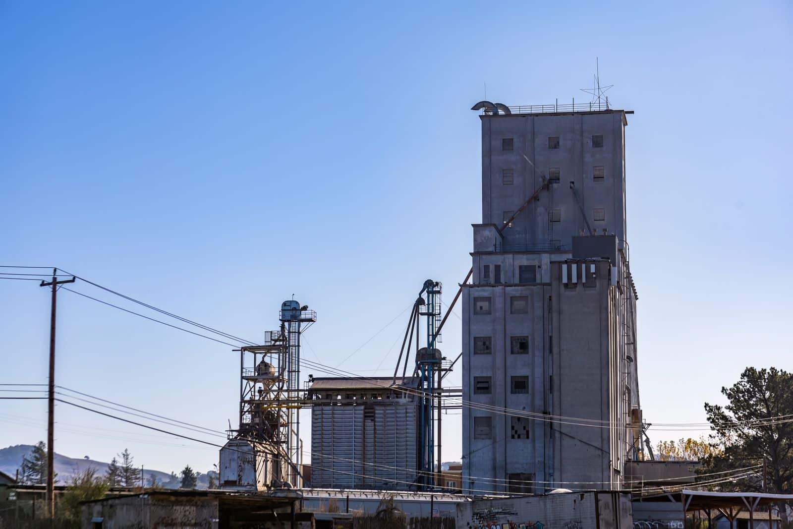 a large clock tower towering over a city Industrial plant with grain elevator towers and a flat-roofed metal building